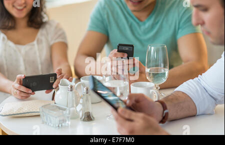Hispanic friends using cell phones in cafe Stock Photo