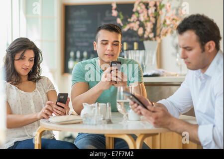 Hispanic friends using cell phones in cafe Stock Photo