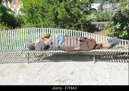 A homeless man sleeping on a bench in Peter Minuit Plaza in Lower Manhattan, New York City. Stock Photo