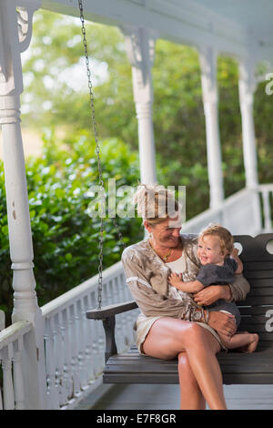 Caucasian mother and toddler sitting in swing on porch Stock Photo