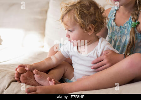 Caucasian girl and toddler brother sitting on bed Stock Photo
