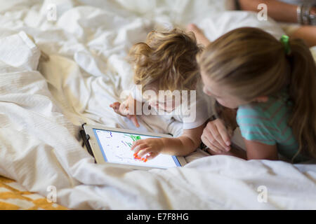 Caucasian girl and toddler brother using tablet computer on bed Stock Photo