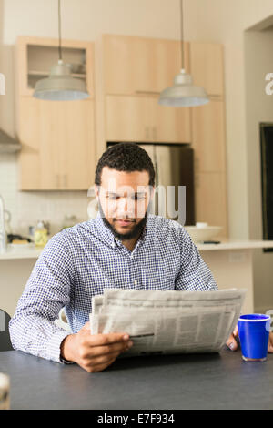 Mixed race man reading newspaper at breakfast table Stock Photo