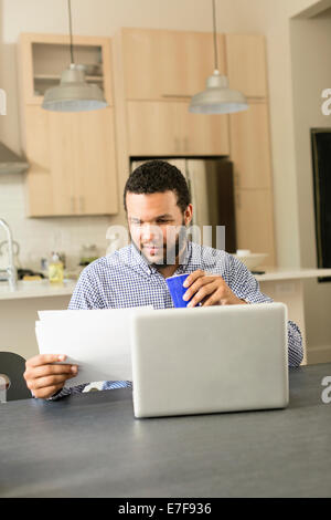 Mixed race man reading at breakfast table Stock Photo