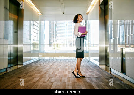 Mixed race businesswoman waiting for elevator in lobby Stock Photo