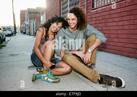 Couple sitting on skateboard on city street Stock Photo