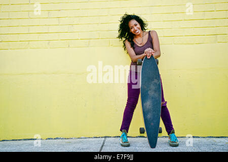 Hispanic woman holding skateboard on city street Stock Photo