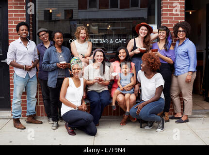 Friends sitting together outside coffee shop on city street Stock Photo