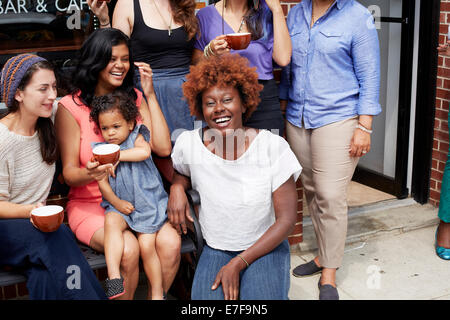 Friends sitting together outside coffee shop on city street Stock Photo