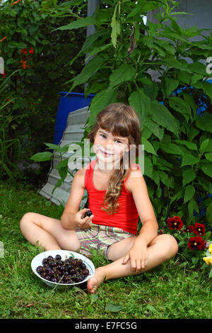 Cute little girl with cherries in garden Stock Photo