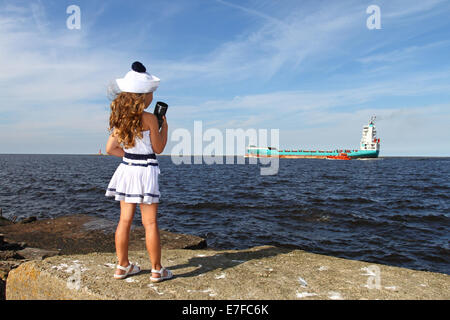Girl on pier at sea with a spyglass looks at ship Stock Photo