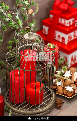 christmas decorations, gift box, red candles, cookies, nuts and spieces on wooden background. vintage style home interior with p Stock Photo