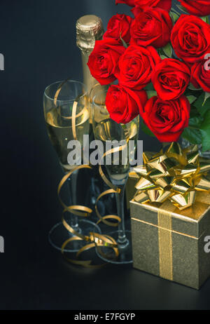 red roses, golden gift box and and champagne on black background. Stock Photo