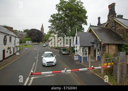 White car stopped on road in village, waiting by lights and boom gate at railway level crossing for train to pass by Stock Photo