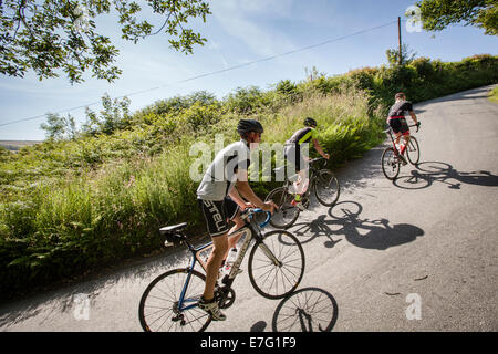 Three cyclists ride up a steep path in Pembrokeshire, Wales Stock Photo