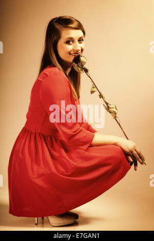 Beautiful fashion woman teen girl in red gown with dry rose. Photo in old color image style. Stock Photo