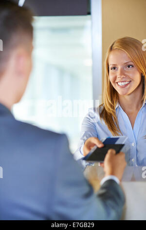 Attractive young woman giving documents to businessman at airport check-in counter Stock Photo
