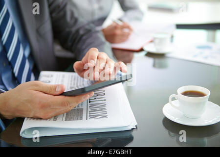 Hands of businessman using digital tablet with newspaper and cup of coffee near by Stock Photo
