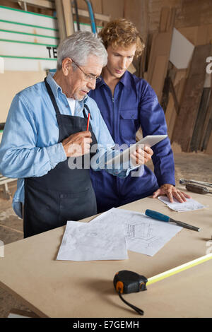 Carpenter Using Digital Tablet With Coworker Stock Photo