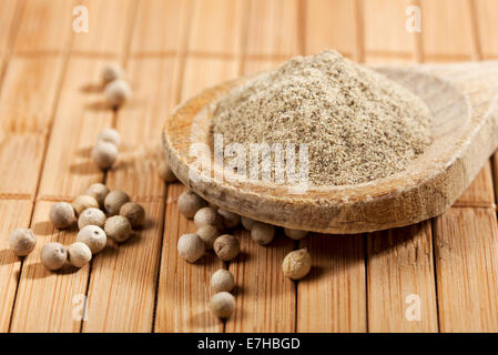 ground white pepper on wooden spoon surrounded by pepper corns on bamboo mat Stock Photo