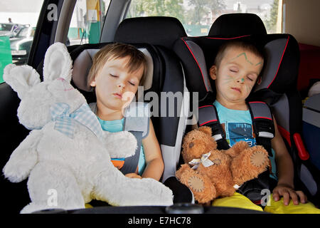 Two boys in car seats, traveling, sleeping in the car with teddy bears Stock Photo