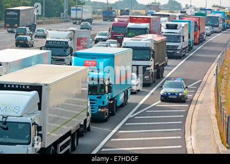 Essex Police BMW car using the hard shoulder to reach accident location at front of gridlocked UK motorway lorry truck & car traffic Stock Photo