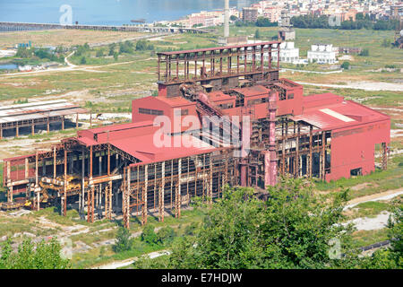 View from above derelict empty factory at Italsider steelworks industrial building with apartment housing distant Bagnoli Naples Napoli Campania Italy Stock Photo