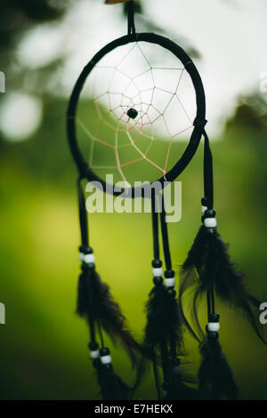 Black dream catcher on green natural background seinging in the wind. Selective focus. Stock Photo