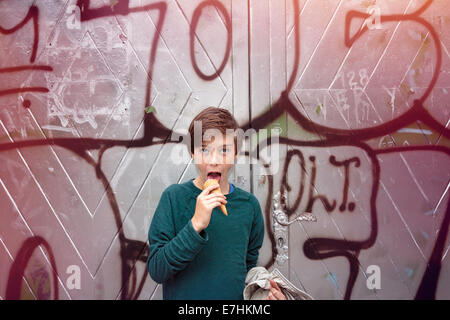 teenager boy in front of a big graffiti is eating his ice cream. Stock Photo