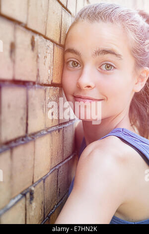 portrait of a smiling teenager girl leaning against a brick wall.