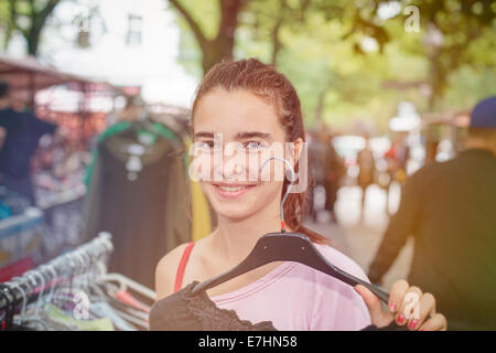 smiling woman on a flea market is holding a clothes hanger. Stock Photo