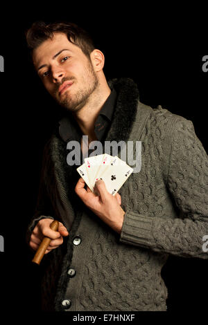Young man holding cards and smoking cigar, isolated over black background Stock Photo