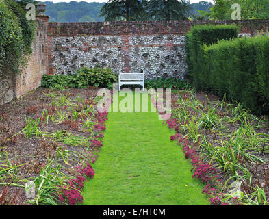 Walled garden with grassy path leading to a white bench seat Stock Photo
