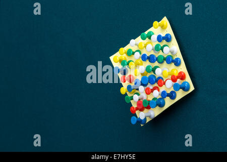 Yellow post-it note with many push pins on a green board Stock Photo