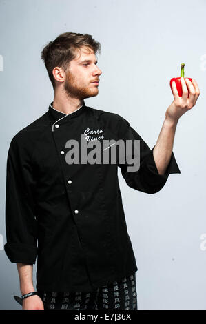 Young chef wearing a chef uniform looking at a bell pepper in his hand Stock Photo
