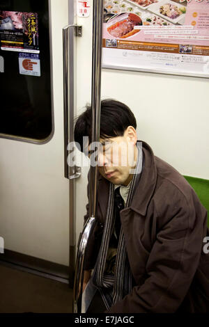 Exhausted Japanese man sleeping on subway train in Kyoto, Japan, Asia. Tired Asian businessman or manager taking a nap while commuting Stock Photo