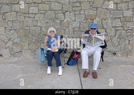 A retired couple sit by a sea wall in Falmouth, Cornwall, UK Stock Photo