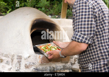 earth clay cob oven.  Now the oven has been built its time to start cooking.  The first dish of herb vegetables  to be roasted Stock Photo