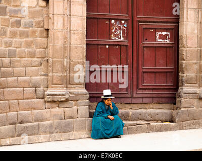 Typical Quechua woman stiitng in fron of a door - Cusco, Peru Stock Photo