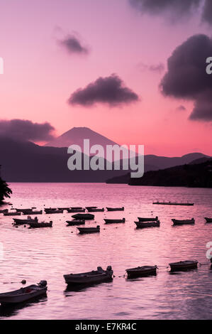 Boats drift in lines along Lake Ashi with Mount Fuji in the background and colorful sunset. Stock Photo