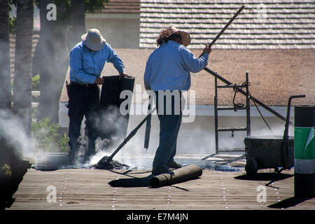 Steam rises from hot tar as Hispanic workmen replace a garage roof in Laguna Niguel, CA. Note rolls of tar paper. Stock Photo