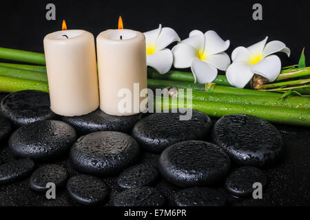 spa concept of zen basalt stones, three white flower frangipani, candles and natural bamboo with drops, closeup Stock Photo