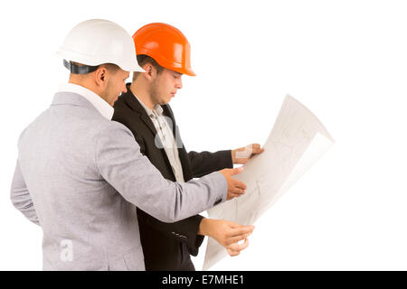 Two young engineers or architects or structural engineers in hardhats and suits standing discussing a building plan or blueprint Stock Photo