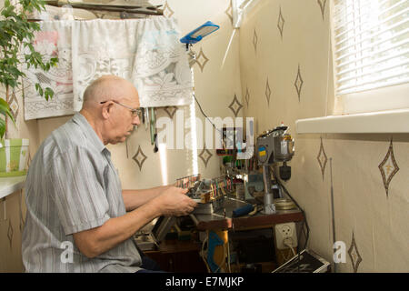 Retired man working at home on his handicrafts sitting at a compact workbench in his house using precision tools and small scale electrical equipment and power tools. Stock Photo