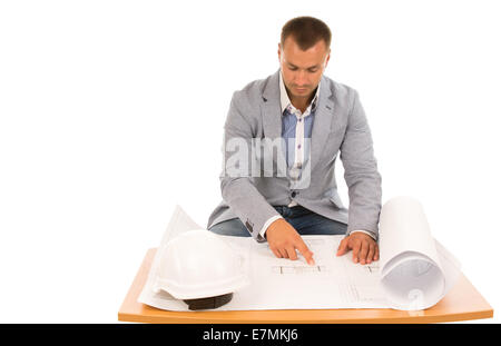 Construction foreman or engineer working on a blueprint sitting at a table reading specification with his hardhat alongside, iso Stock Photo