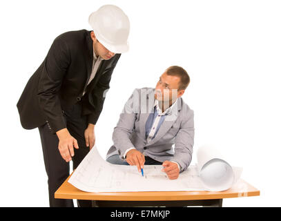 Building foreman and architect discussing a plan or blueprint with one standing looking down and the other seated pointing to a  Stock Photo