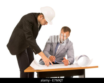 Two building contractors discussing a blueprint of a project they are working with one seated in front of the plan and the other Stock Photo