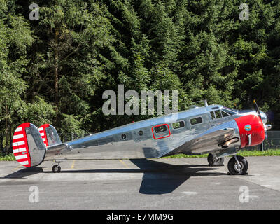 A veteran Beechcraft Twin aircraft (Beechcraft Model-18) parked against a background of trees. Stock Photo