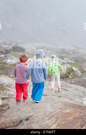 Three kids walking down a rocky mountain trail Stock Photo