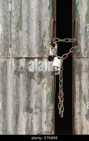 Chained tensile steel high security padlock on painted galvanized corrugated warehouse with doors slightly ajar Stock Photo